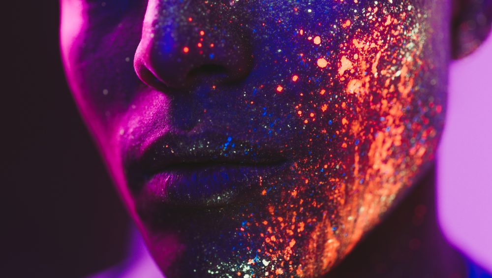 Cropped image of face with neon paint splashes on skin.