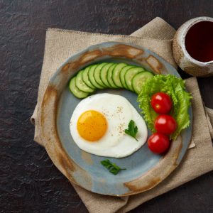 Food on plate, fried egg, slices of cucumber, tomato and lettuce.