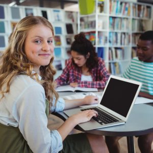 Sirl smiling while using laptop at table with other students in library.