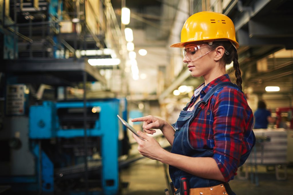 Engineer in factory with yellow hard hat and digital tablet.