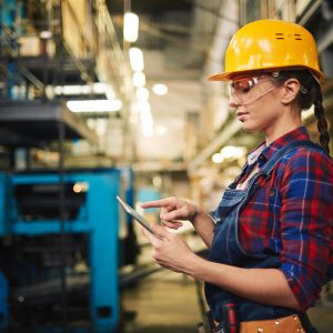 Engineer in factory with yellow hard hat and digital tablet.