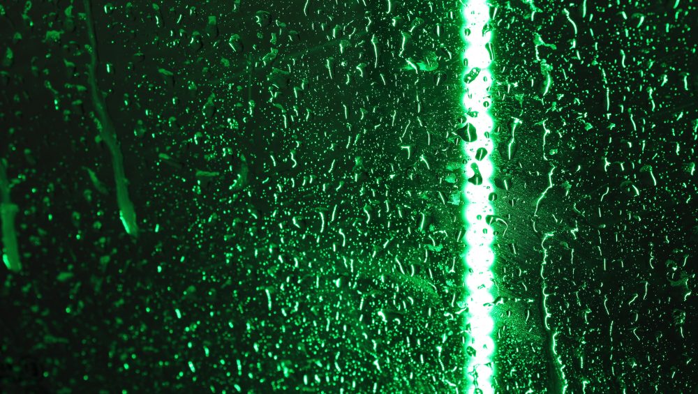 Background image of green neon light though window covered in rain.