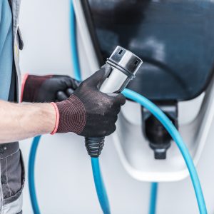 Person with gloved hands holding electric car charging plug.