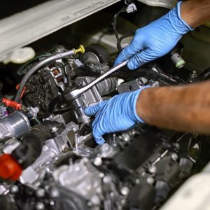 Hands in blue gloves working on car engine
