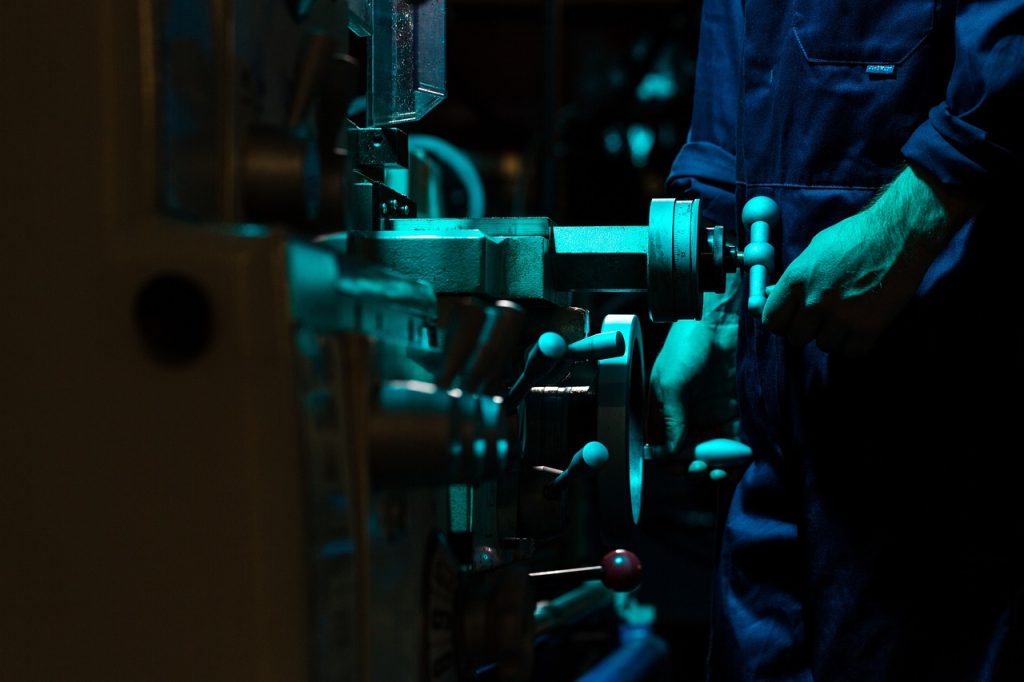 Person in overalls turning tap on pipe