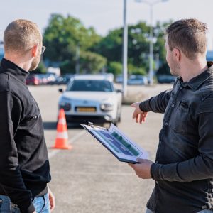 Two men standing with a clipboard pointing at car