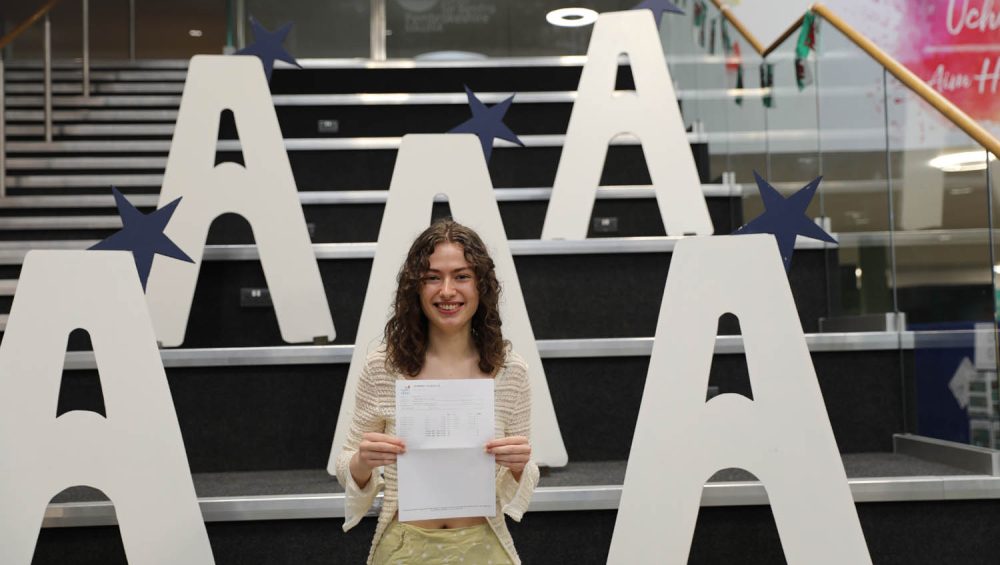 Madeleine Draycott holding results, large a's in background on stairs.