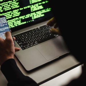 person looking at computer code on phone and typing into laptop