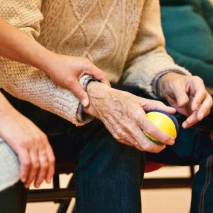 older hands holding a ball, with younger hands gently holding arm