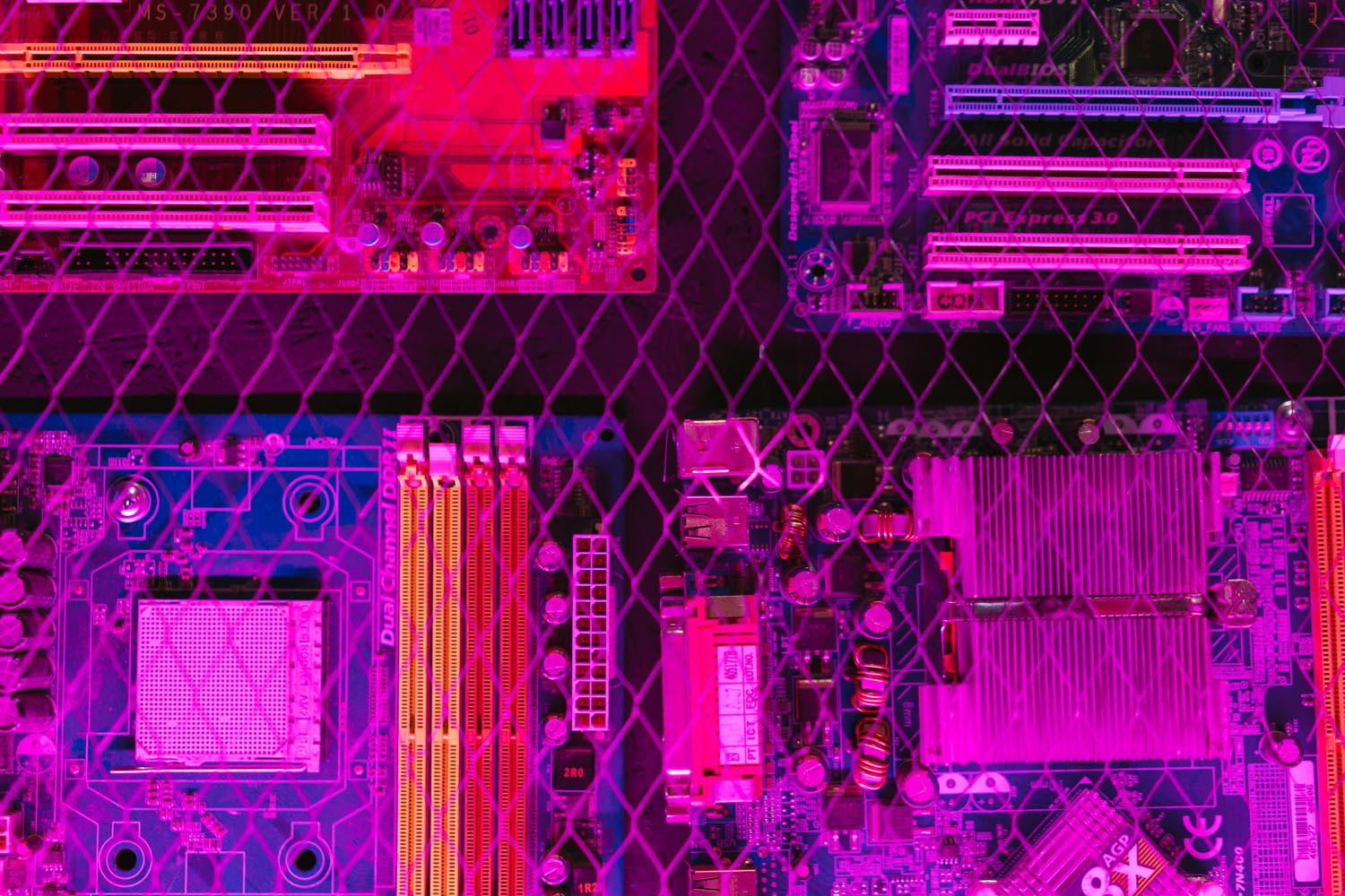 Computer motherboards behind wire fence lit with neon lights