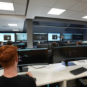 Learners looking at the screen in the Control Room. Teacher at the front of the class