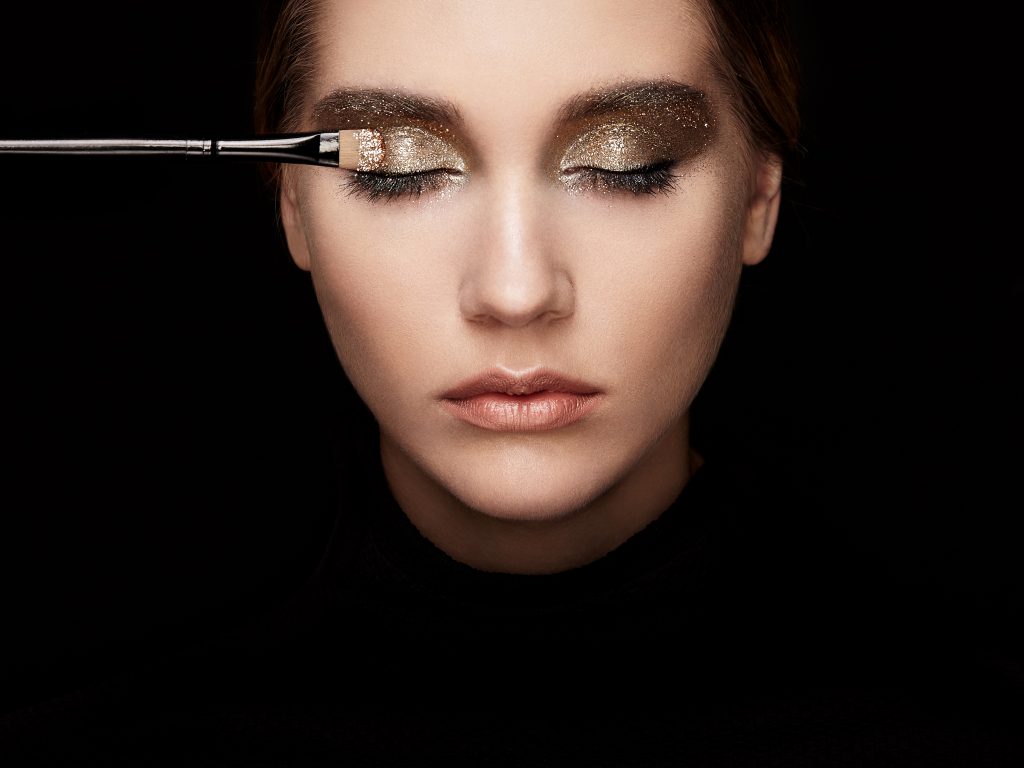Womans face with eyes closed and gold eye shadow being applied