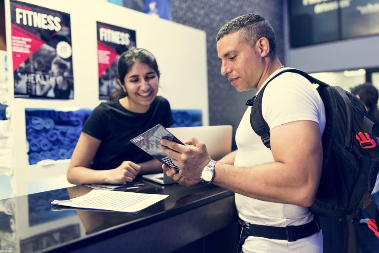 man wearing rucksack looking at flyer, person behind a counter