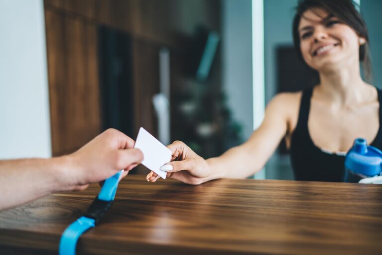 Cheerful woman talking to employee on reception taking card for access in gym