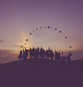 Silhouetted students on a hill throwing graduation caps.