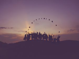 Silhouetted students on a hill throwing graduation caps.