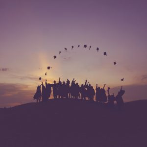 Silhouetted students on a hill throwing graduation caps.
