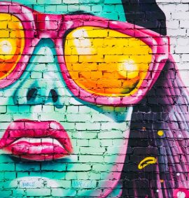 Graffiti on brick wall of woman's face wearing sunglasses.