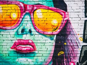 Graffiti on brick wall of woman's face wearing sunglasses.