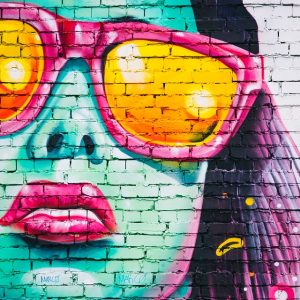 Graffiti on brick wall of woman's face wearing sunglasses.