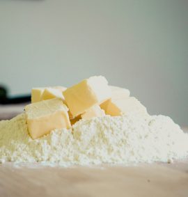 Cubes of butter on a mound of flour on wooden surface.