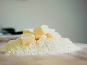 Cubes of butter on a mound of flour on wooden surface.