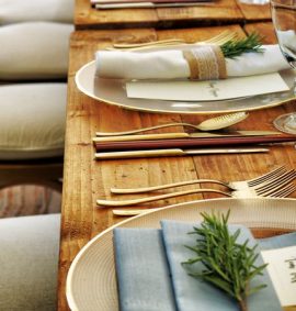 Formal table setting on wooden table with gold cutlery and rosemary placed on the napkins.