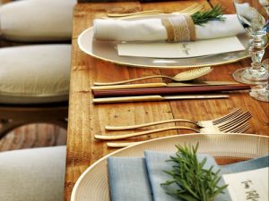 Formal table setting on wooden table with gold cutlery and rosemary placed on the napkins.