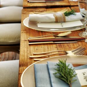 Formal table setting on wooden table with gold cutlery and rosemary placed on the napkins.