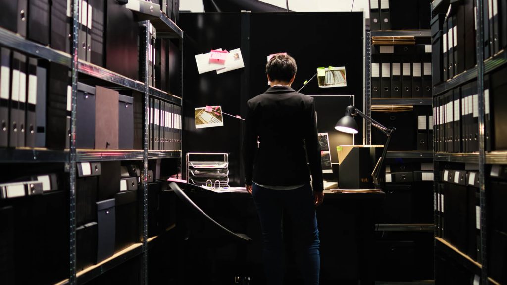 Back of a person in a dark room surrounded by files.