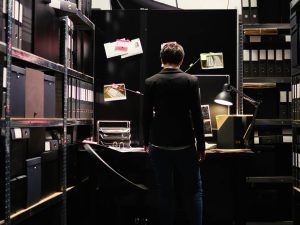 Back of a person in a dark room surrounded by files.