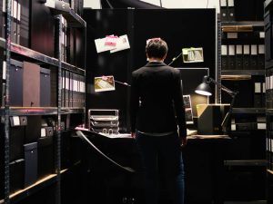 Back of a person in a dark room surrounded by files.