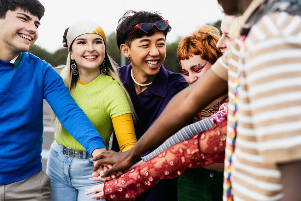 Happy young diverse friends having fun stacking hands together outdoors.