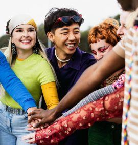 Happy young diverse friends having fun stacking hands together outdoors.
