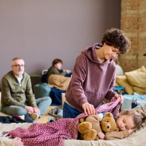 woman covering her sleeping son with teddybear with warm blanket background other temporarily homeless people