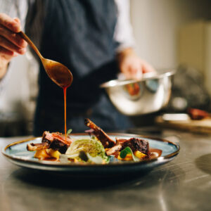 Chef pouring sauce on meal in kitchen.