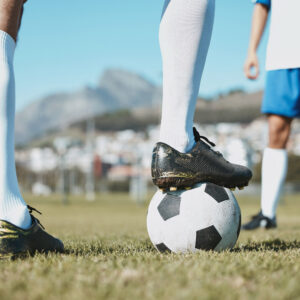Legs on a football pitch, one resting on top of a football.