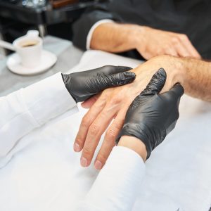 Hands being massaged by beautician wearing black gloves.