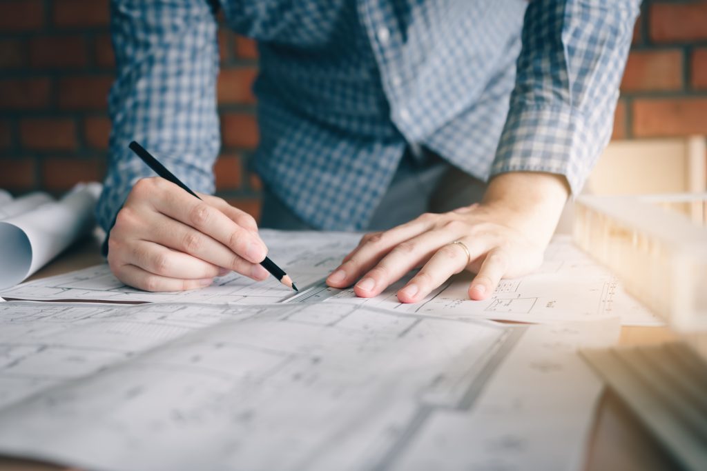 Hands drawing a line with a pencil and ruler on a technical drawing.