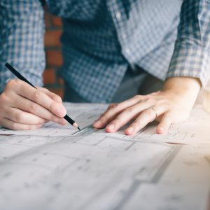 Hands drawing a line with a pencil and ruler on a technical drawing.