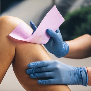 Leg being waxed by beautician wearing blue gloves.