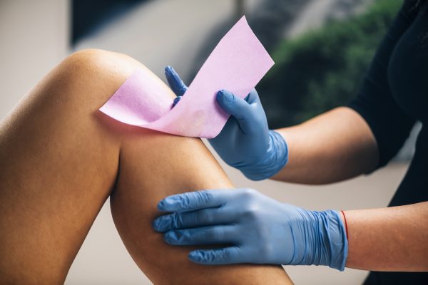 Leg being waxed by beautician wearing blue gloves.