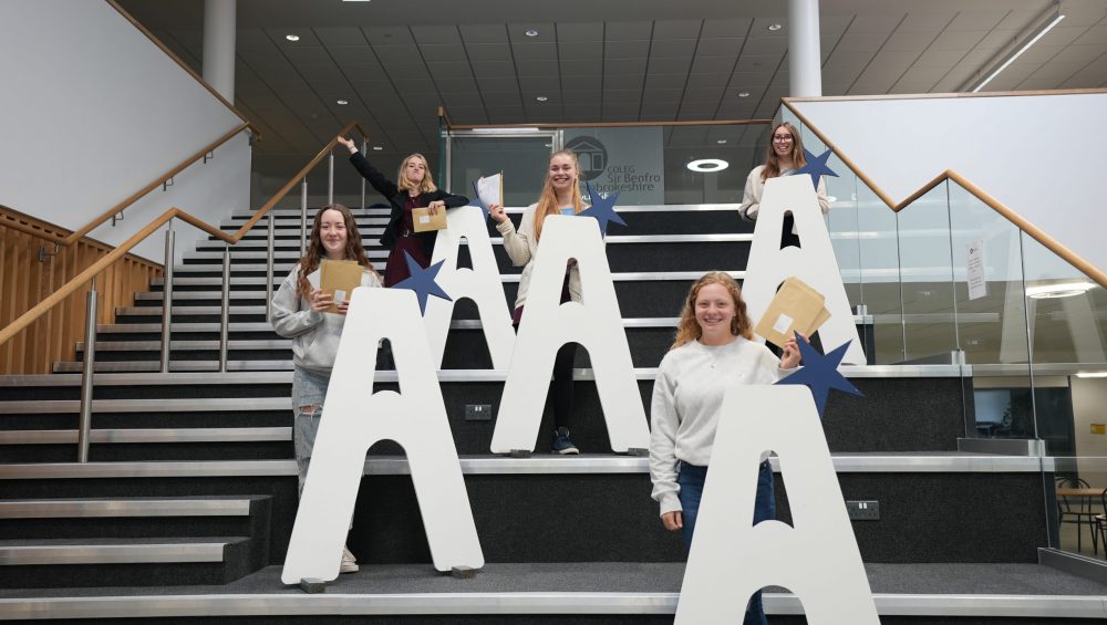 Students standing behind large A's on stairs and holding results envelopes.