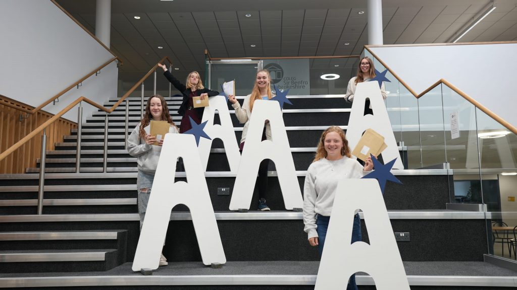 Students standing behind large A's on stairs and holding results envelopes.