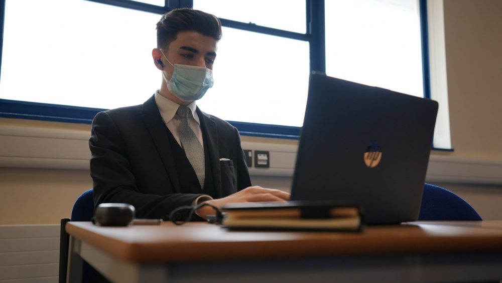 Student wearing mask siting and using laptop.