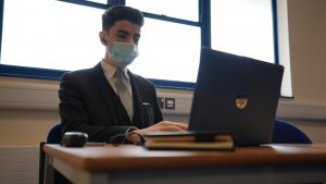 Student wearing mask siting and using laptop.