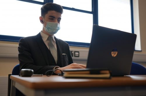 Student wearing mask siting and using laptop.