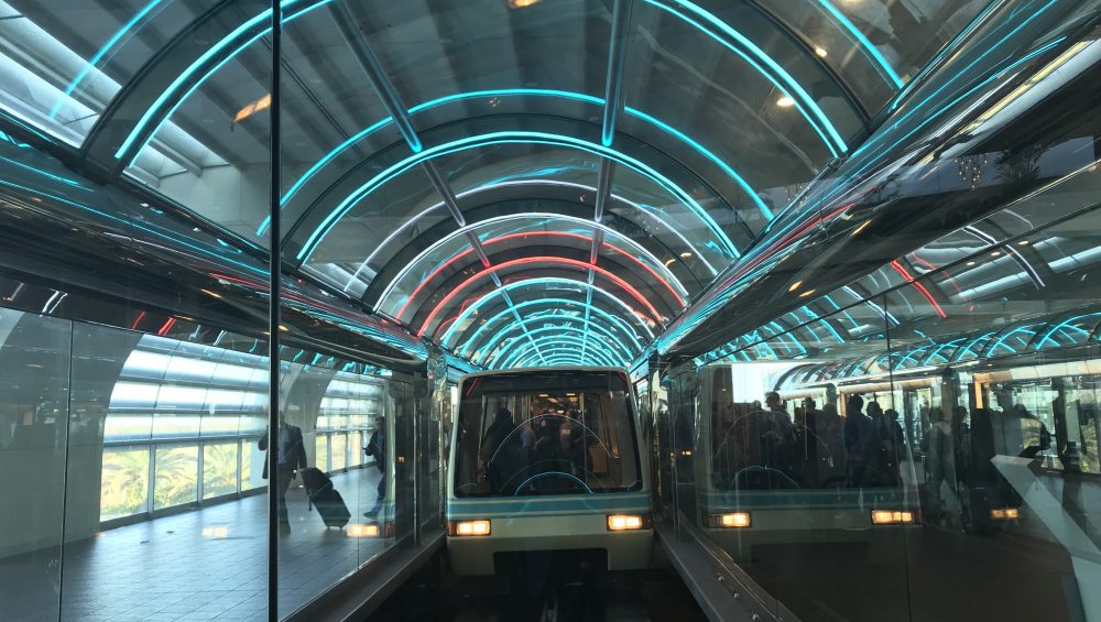 Train in glass tunnel lit by neon lights.