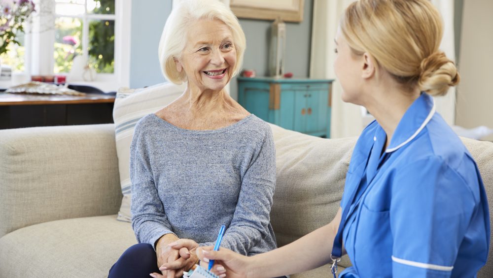 Nurse talking to senior woman on sofa.