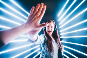 Found smiling woman high-fiving person in foreground, with neon lighting.